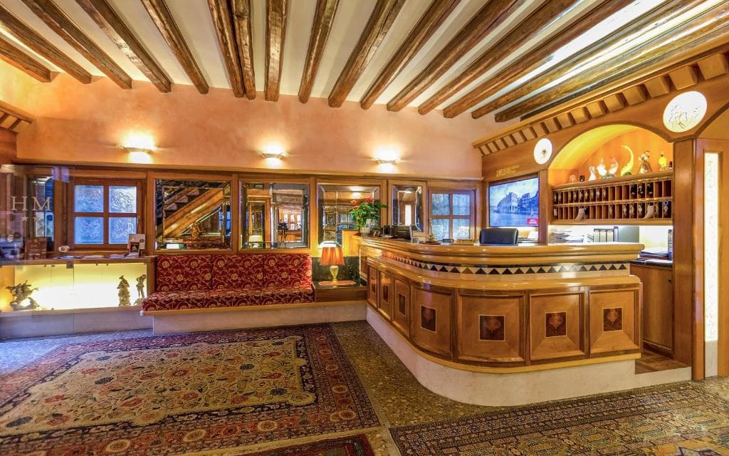 Elegante reception con soffitto a travi, bancone in legno e tappeti orientali decorati.