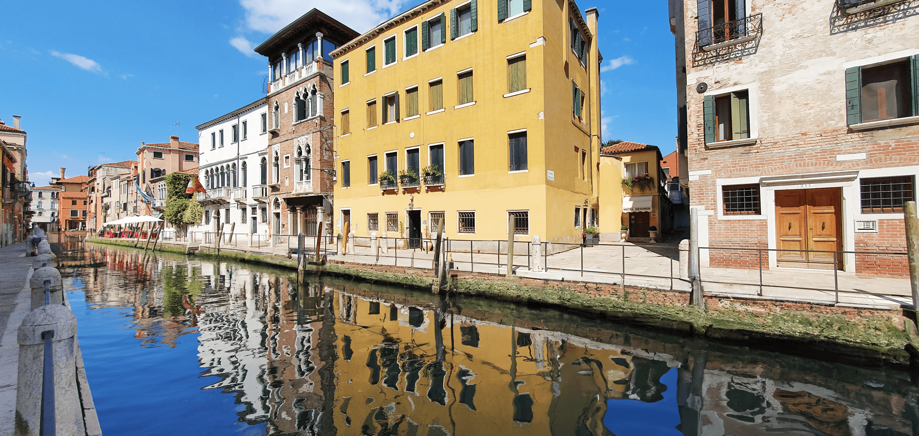 Canale di Venezia con palazzi colorati riflessi nell'acqua sotto un limpido cielo azzurro.